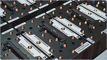 Rows of industrial batteries with black handles and copper connectors, aligned neatly. White labels display technical details, conveying an organized, efficient setup.